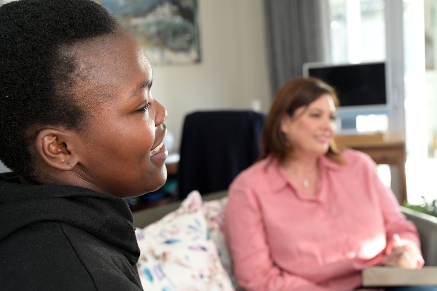 A client's face in warm conversation, Zeldi Hall present, out of focus.